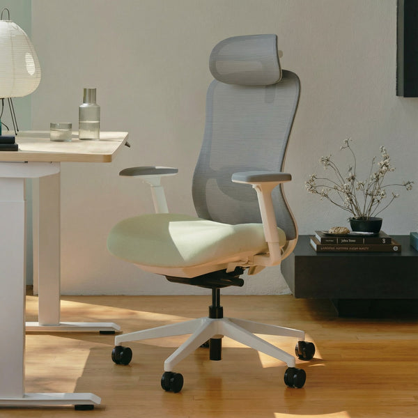 Modern white and green ergonomic office chair in a minimalistic office setting with a height adjustable desk and decor.