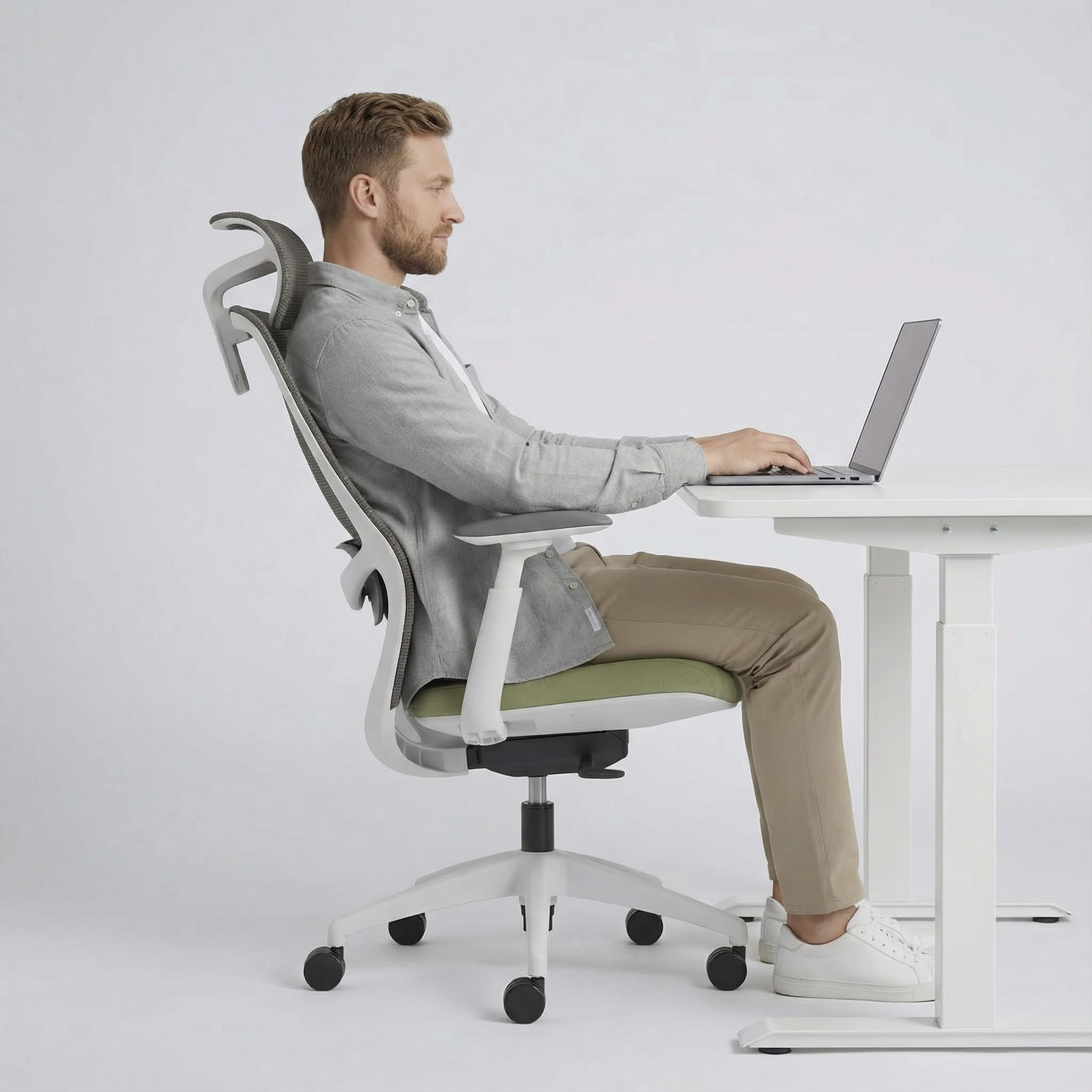 Man sitting on a modern ergonomic desk chair using a laptop at a white sit stand desk.