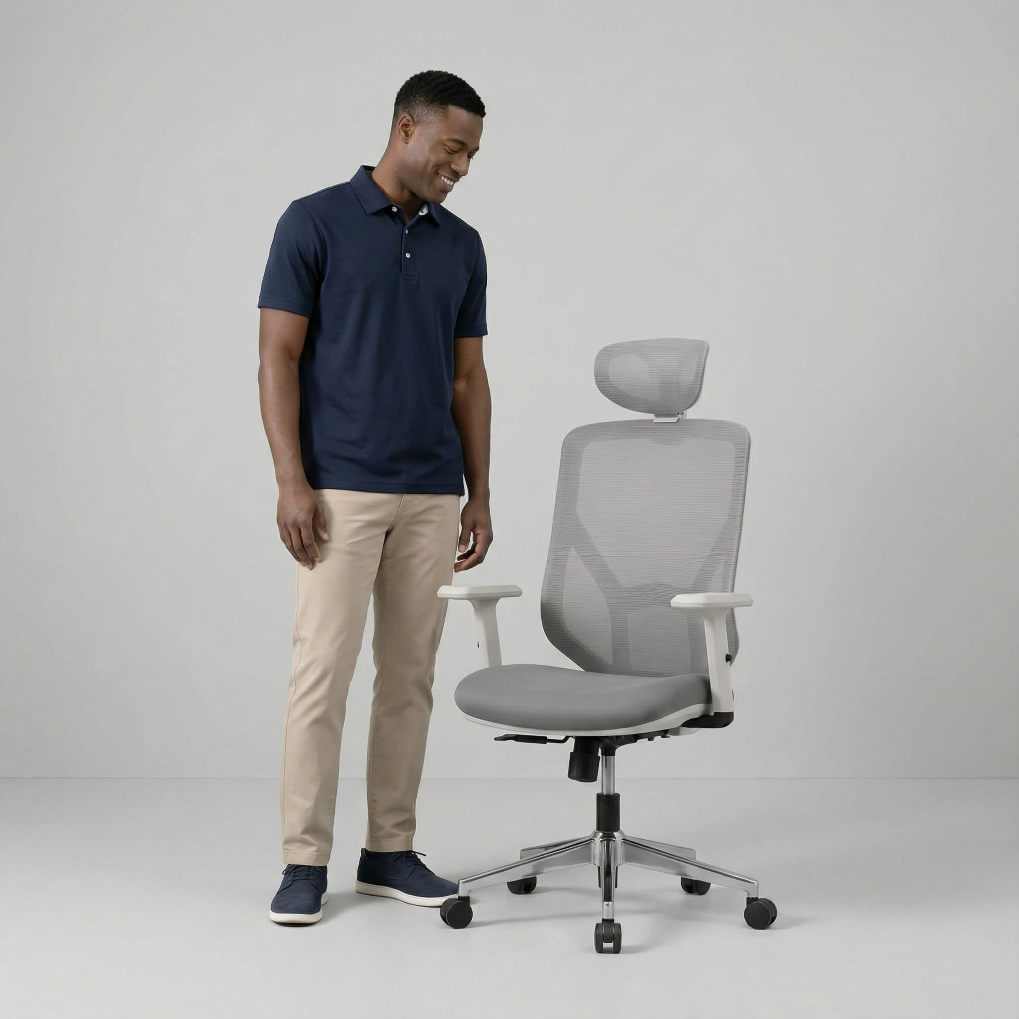 Man standing next to a gray office desk chair with mesh on a plain background 