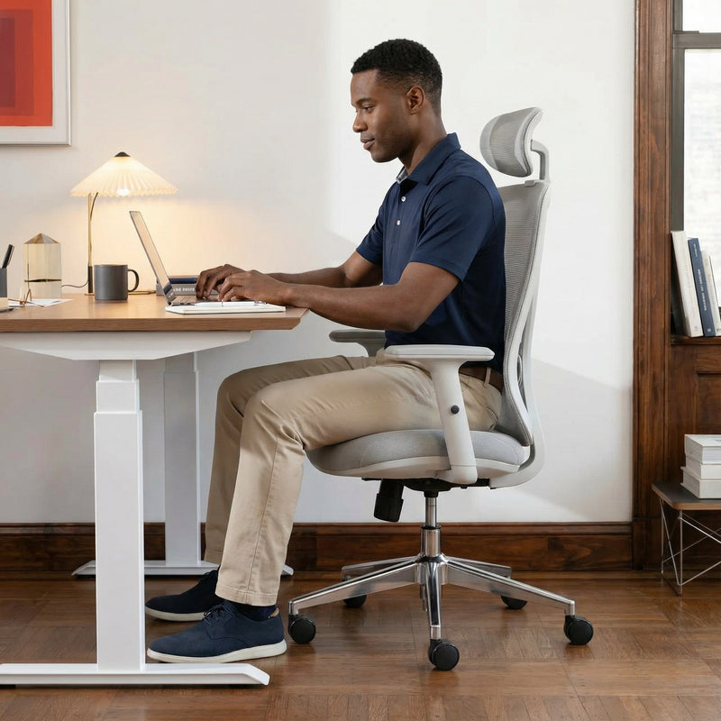 Man sitting at a standing desk using a laptop in a home office setting on ergonomic chair