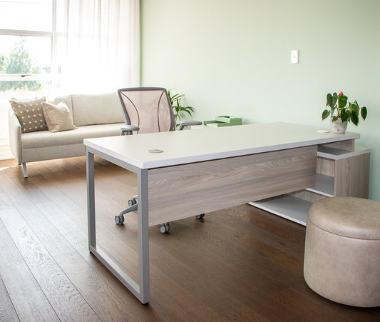 Modern office desk with chair in a bright room with a couch and plants.