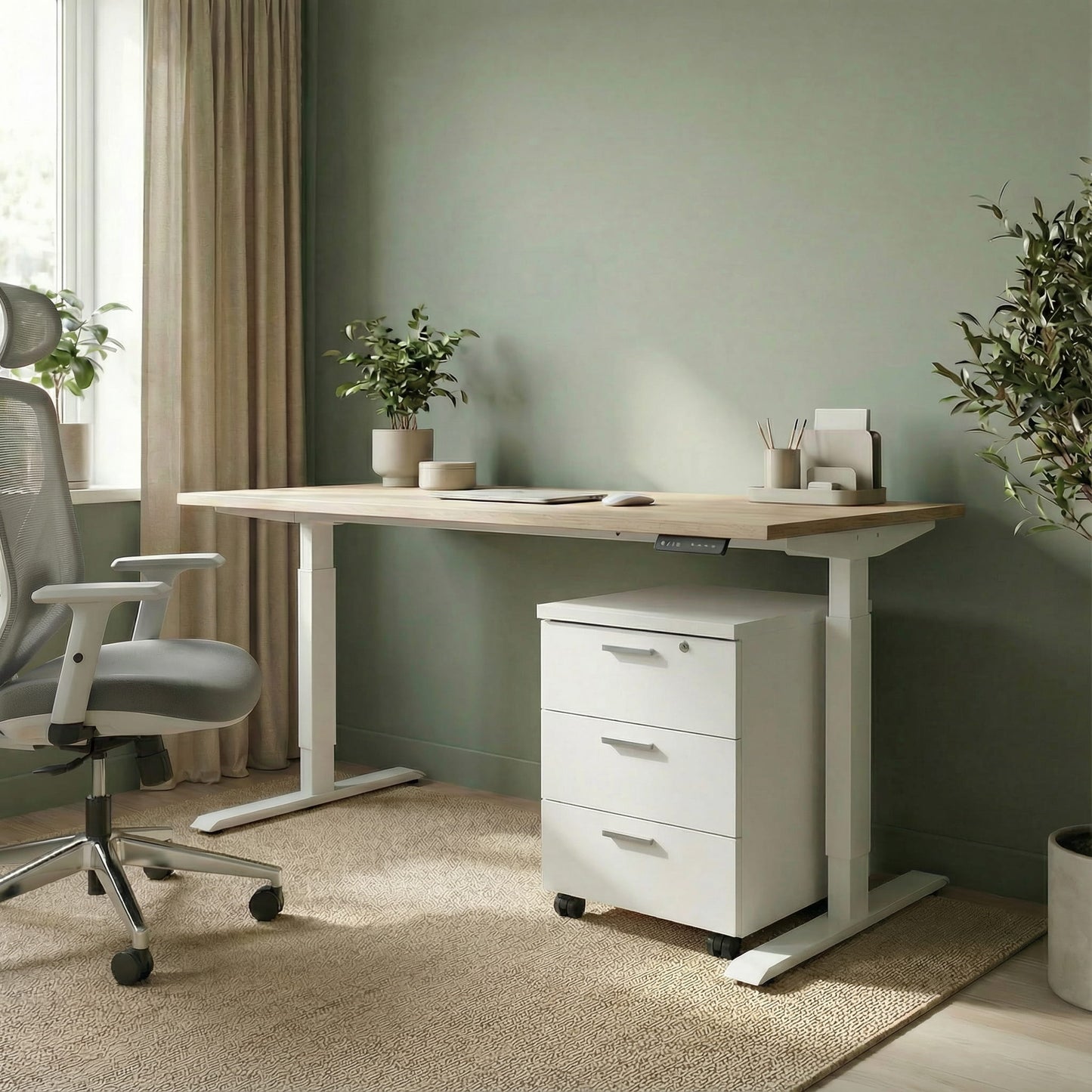 White storage with three drawers on wheels under a white framed sit stand height adjustable desk in a modern office room with a grey office chair and green background 