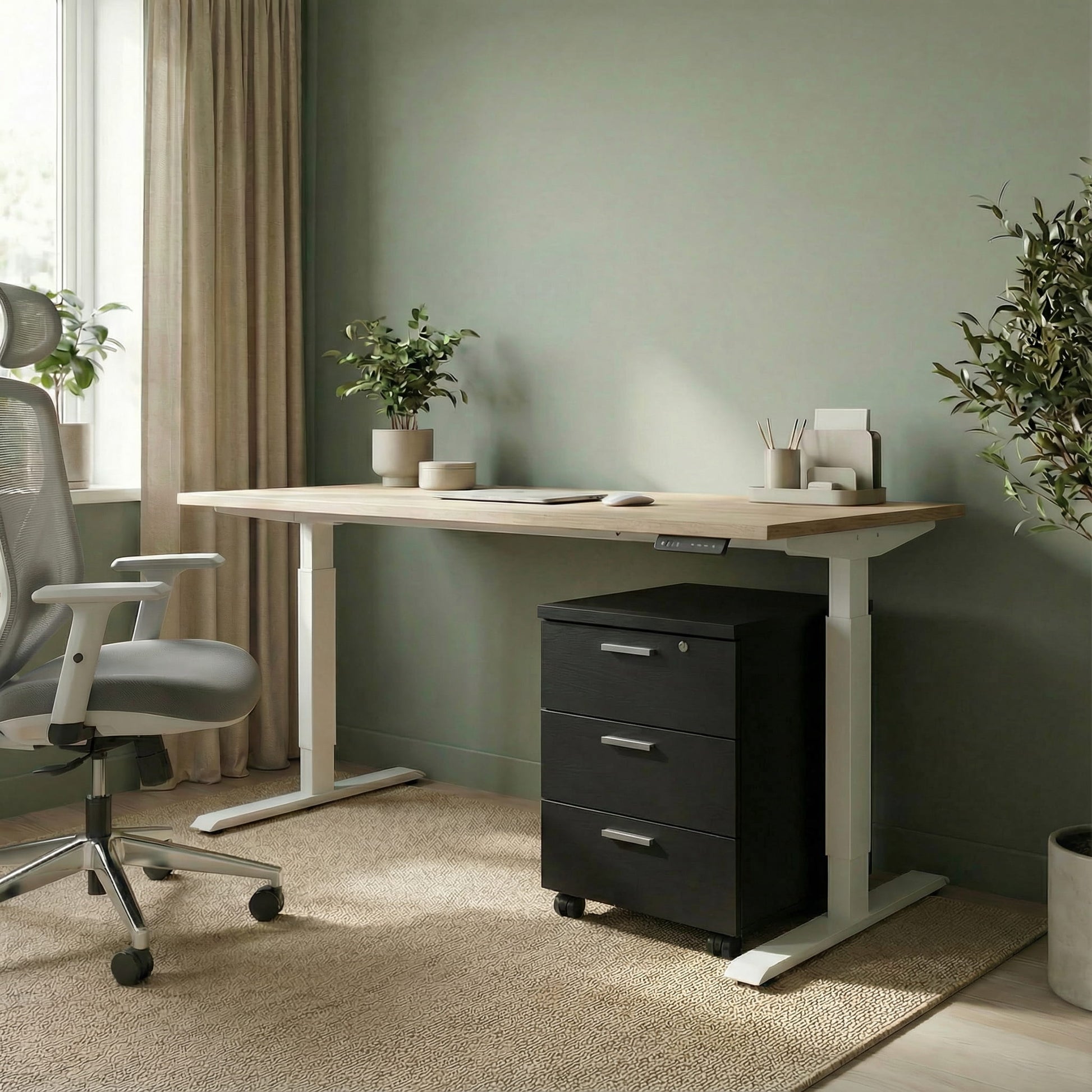 Black storage with three drawers on wheels under a white framed sit stand height adjustable desk in a modern office room with a grey ergonomic chair in the office space