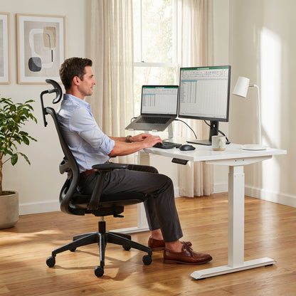 Man sitting at a modern office desk with two monitors and a laptop.