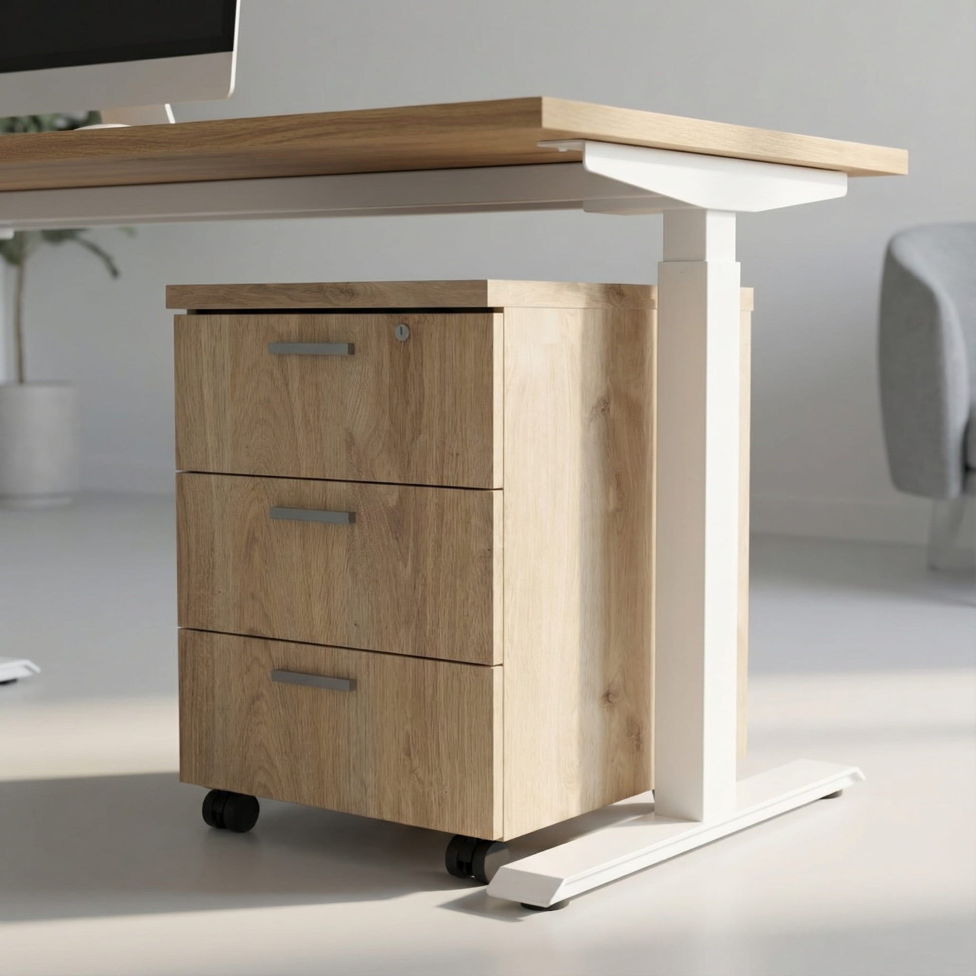 Oak storage with three drawers on wheels under a white framed sit stand height adjustable desk in a modern office room