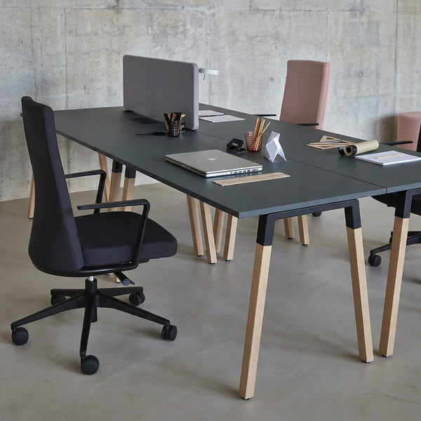 Modern office setup with a long black desk, office chairs, and office supplies against a concrete wall.