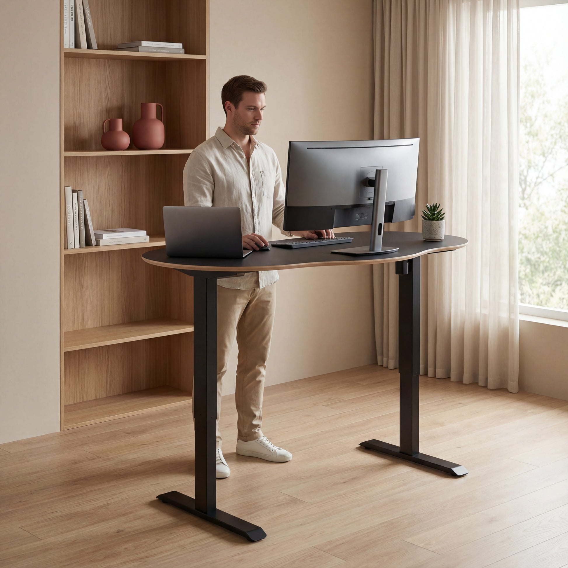 Man using a laptop and desktop computer at a standing desk in a home office setting.